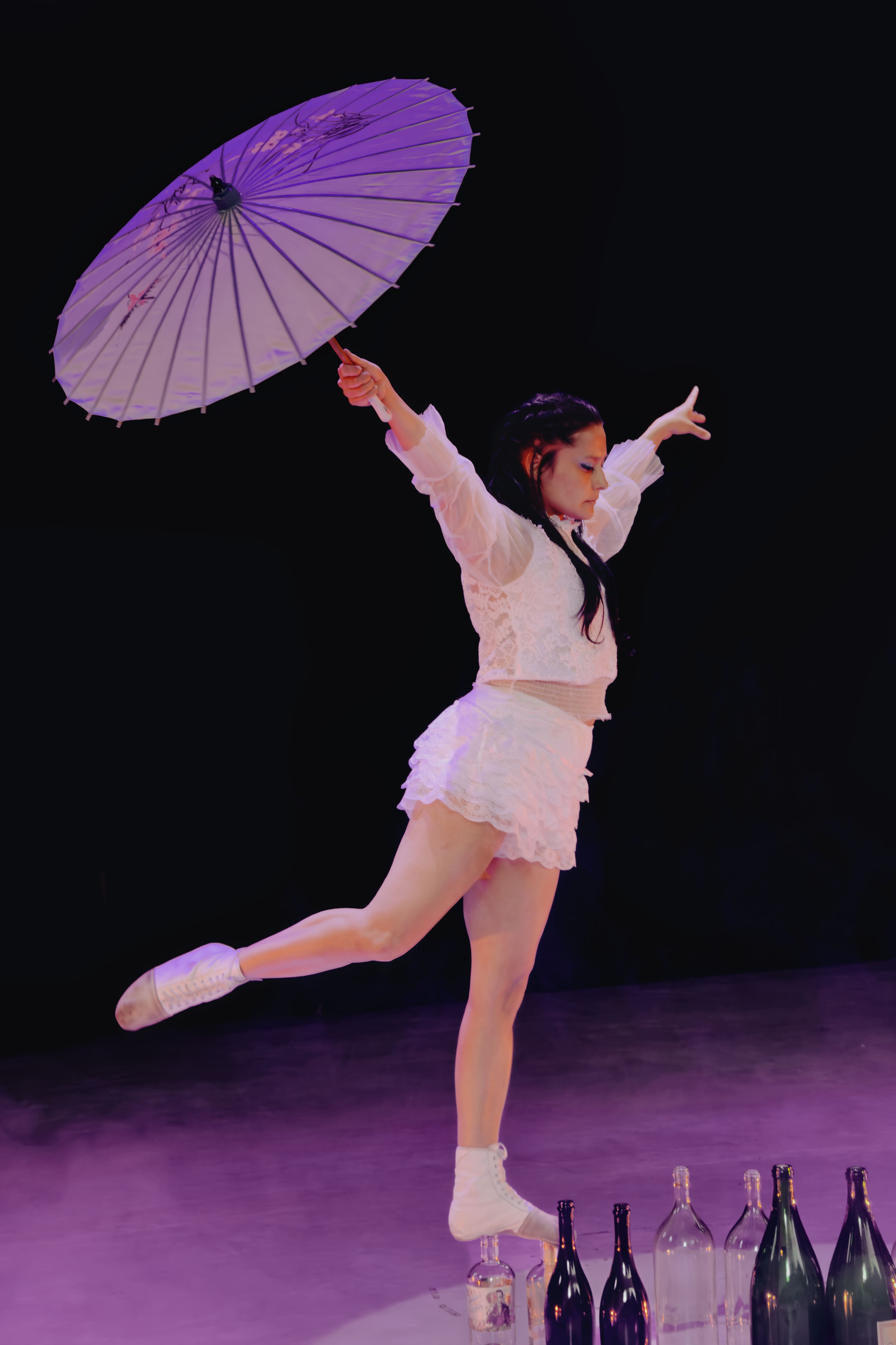 Bailarina con sombrilla morada entre botellas en el escenario