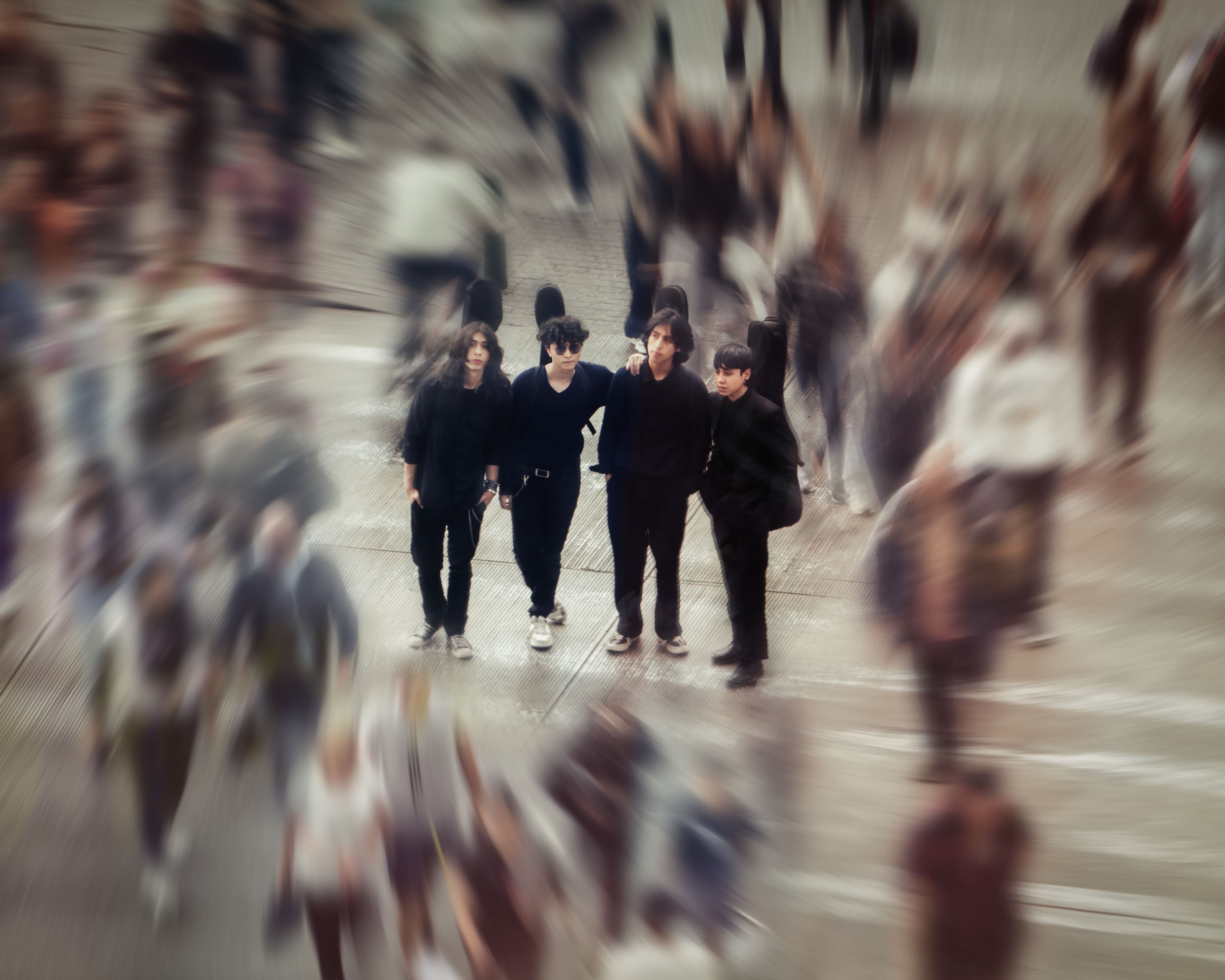 Cuatro personas vestidas de negro en medio de multitud con efecto de zoom