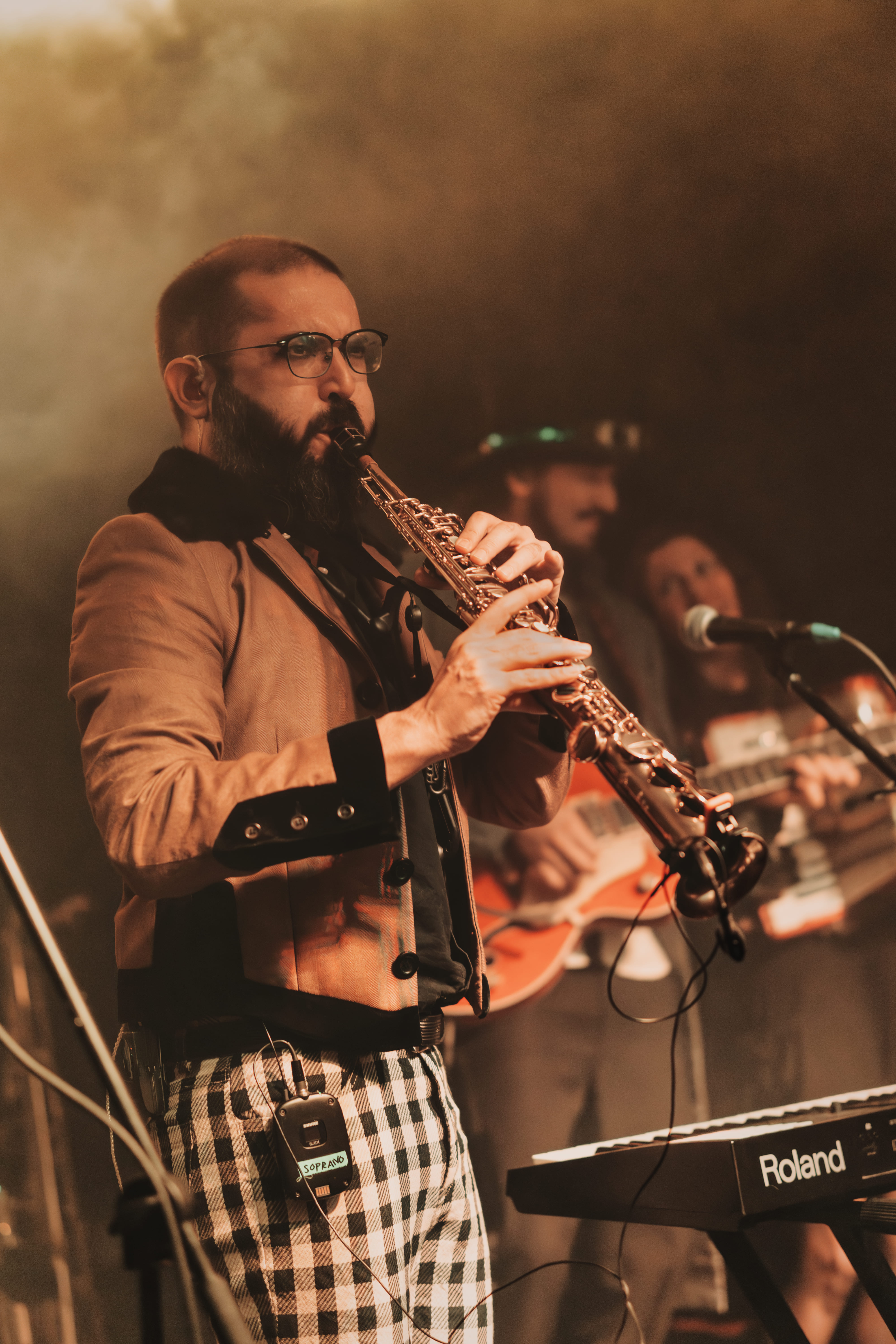 Saxofonista soprano entre humo anaranjado con la banda al fondo