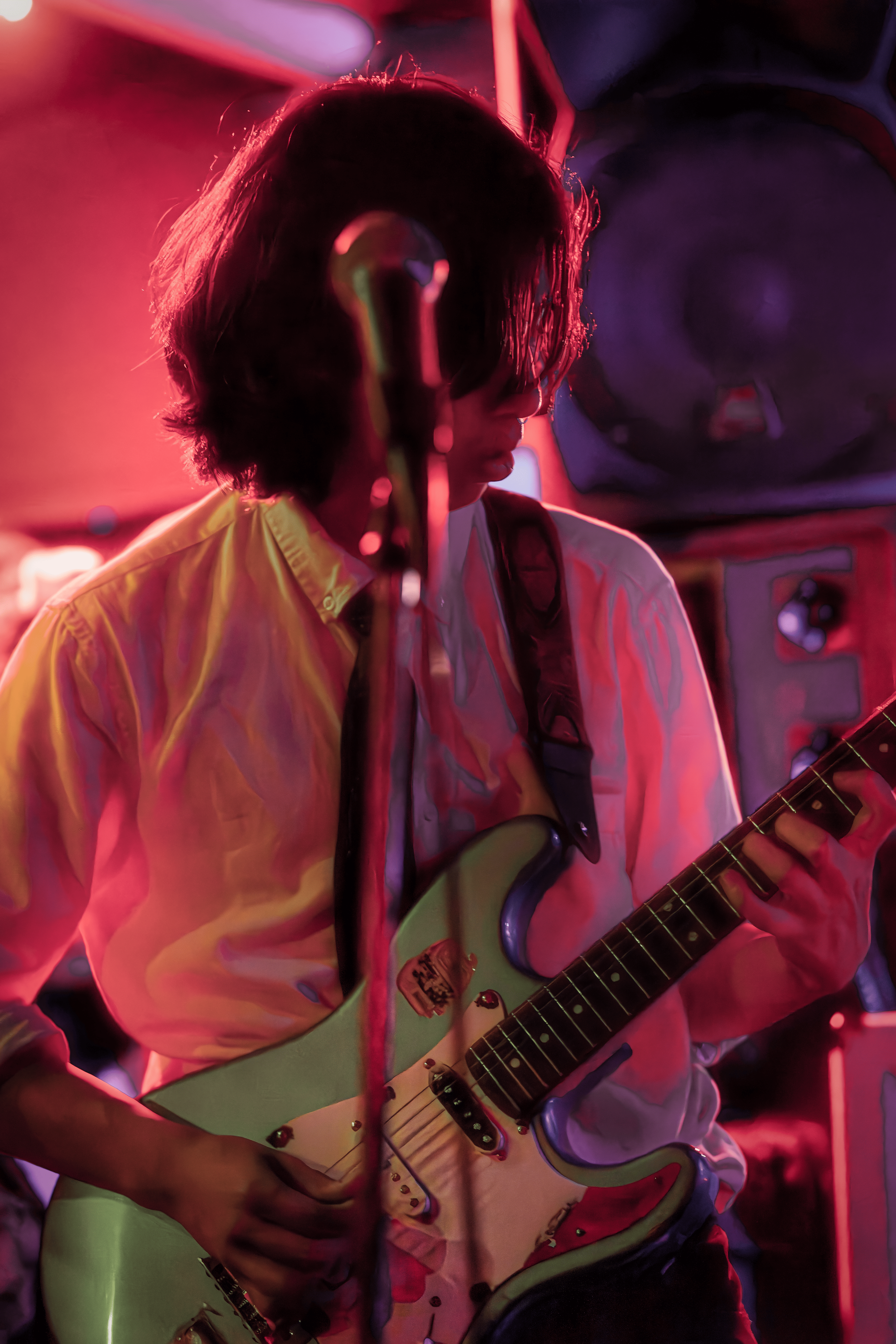 Guitarrista joven con camisa blanca bajo luz roja intensa