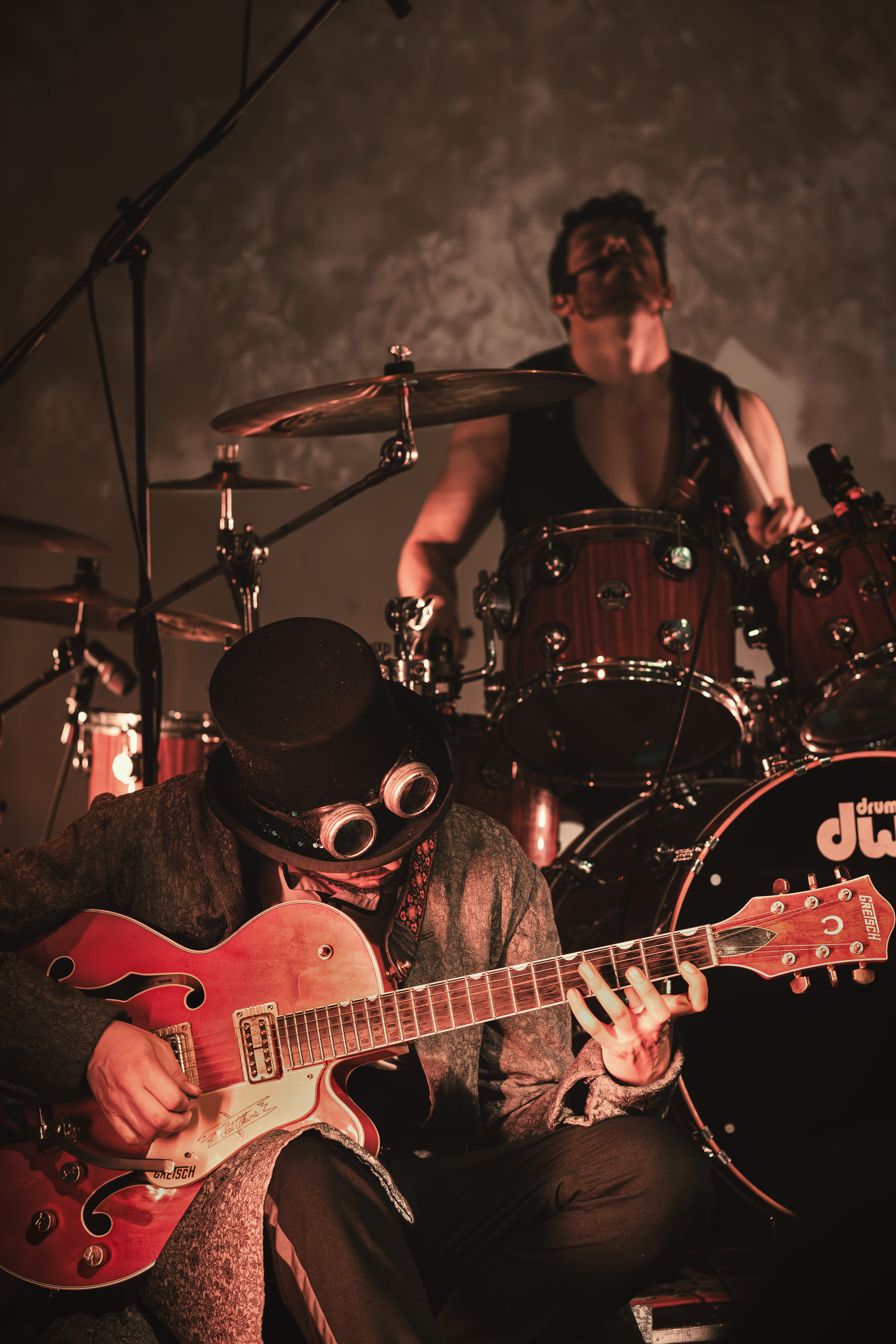 Guitarrista con sombrero y gafas steampunk, baterista al fondo