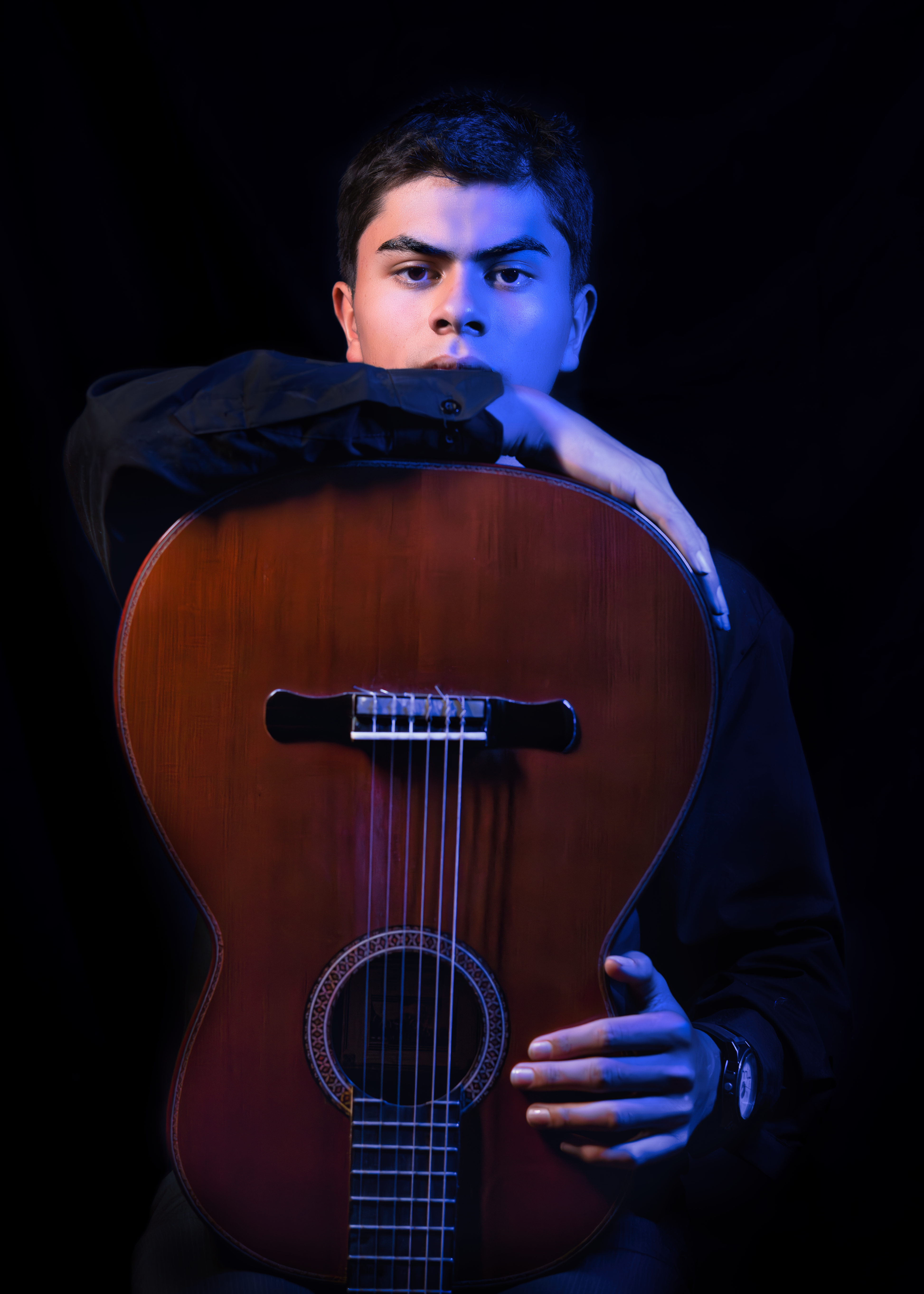 Joven apoyado en guitarra clásica bajo luz azul lateral