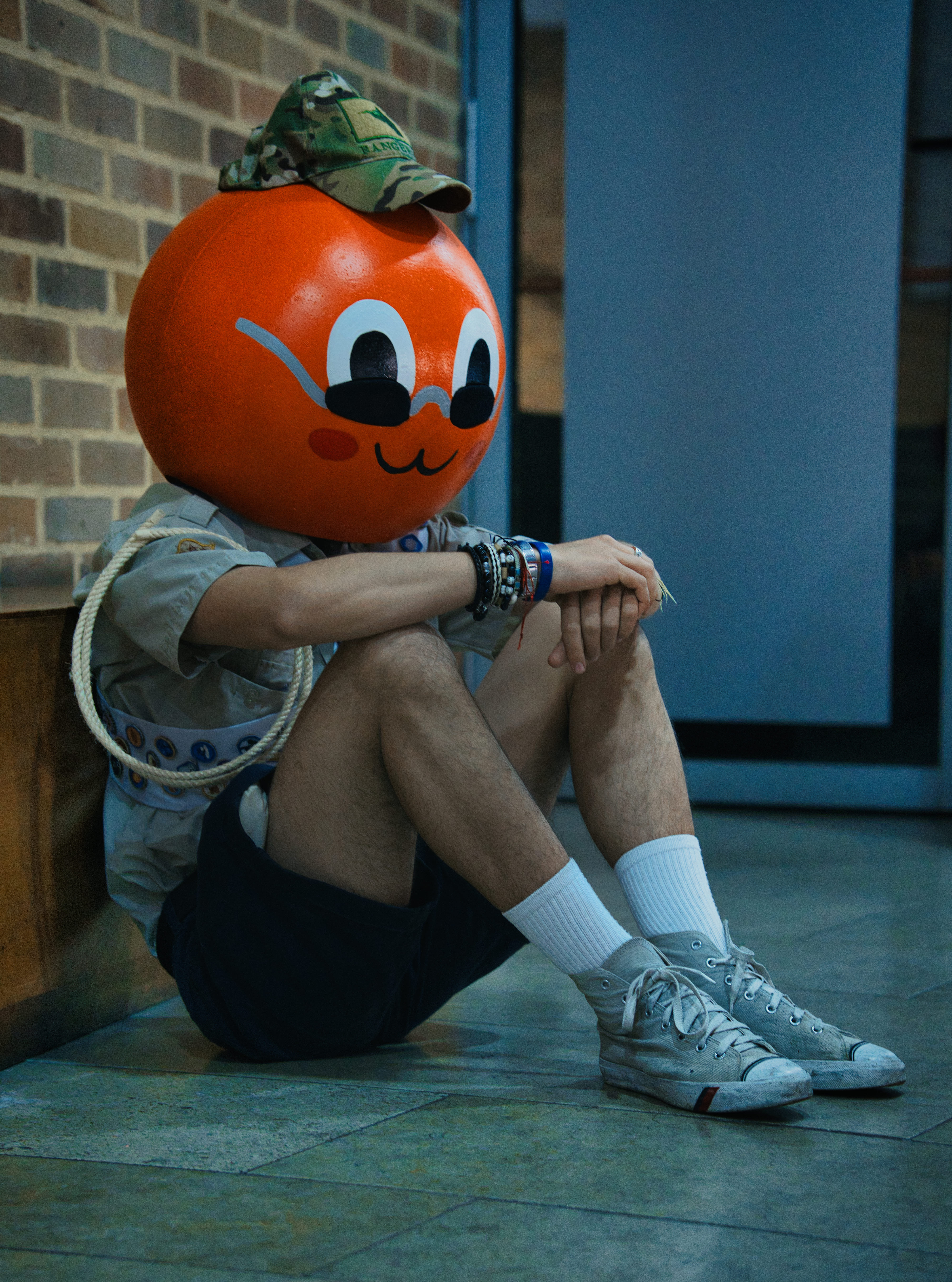 Personaje con cabeza de naranja sentado en el piso