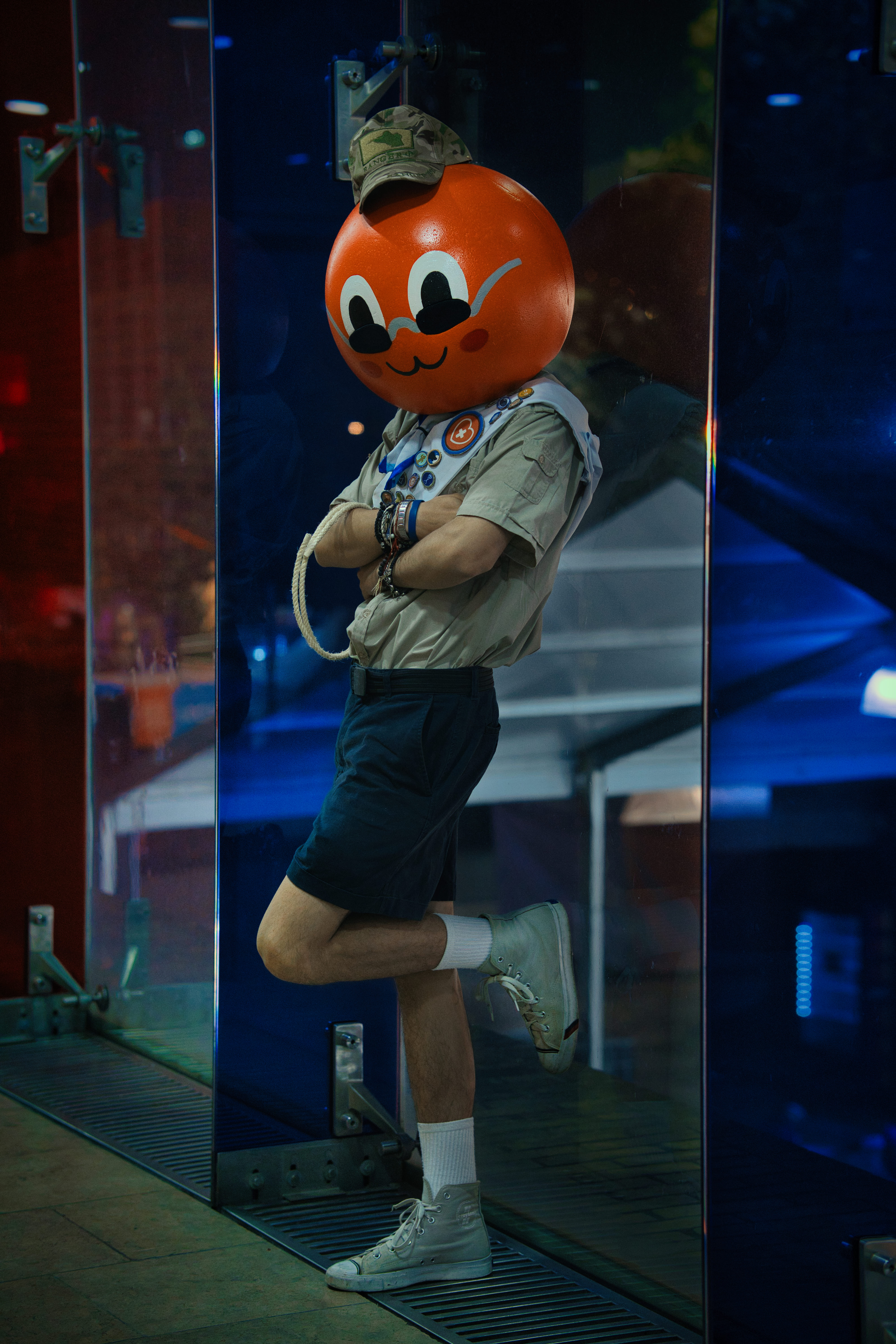 Personaje con cabeza de naranja parado en cabina de vidrio